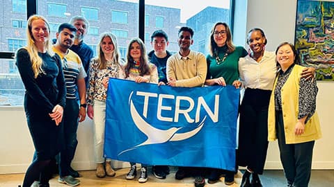 A group of people stood in a row, holding a large blue flag with the TERN logo.