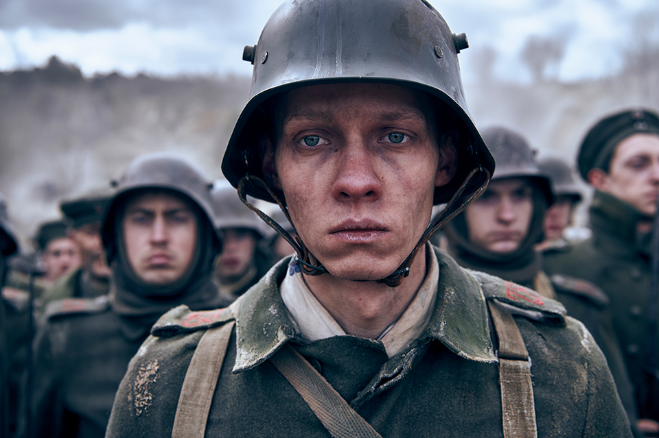 A soldier's face, head and shoulders. He looks into the distance. He is wearing uniform and a helmet. In the background there are other soldiers. Still taken from Netflix film All Quiet on the Western Front. Copywrite - ReinerBajo - Netflix.