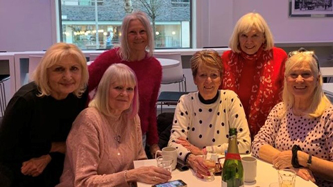 A group of six alumnae sat at a table smiling to the camera