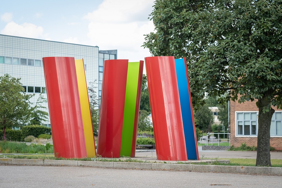 Abstract sculpture: three steel tubes with openings. Outsides are red; insides blue, yellow and green.