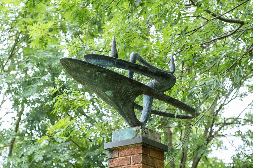 Abstract, swirling bronze sculpture atop brick plinth