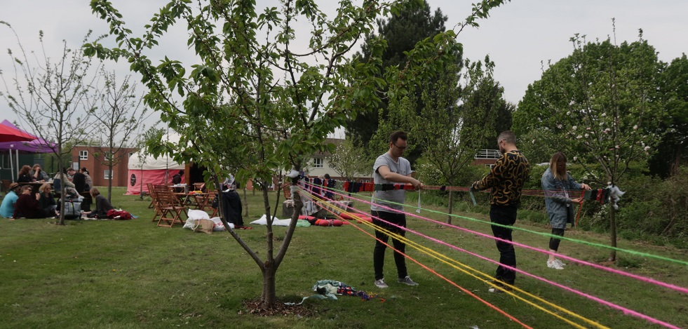 People engaged in activities: they are attaching coloured pieces of string to young trees in a green area