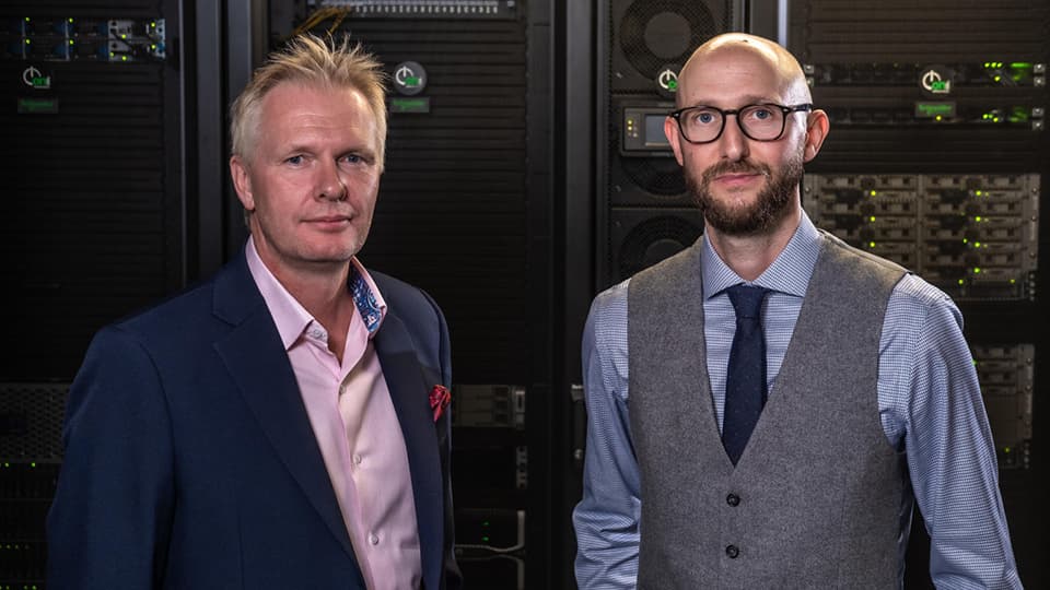 Professors Tom Jackson and Ian Hodgkinson dressed smartly standing in front of a data centre.