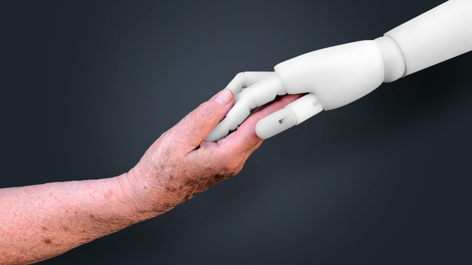 An elderly human hand, holding a robotic hand. 