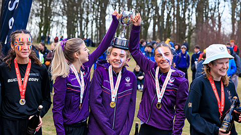 three students with gold medals balancing a trophy on one of their heads
