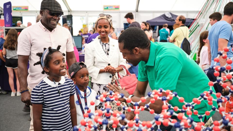 Two adults and two children smiling and talking to a researcher at an exhibition stand. 