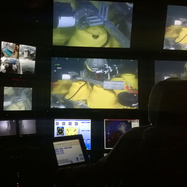 Inside the control room of the Vector, looking over the shoulder of a researcher towards a bank of video screens