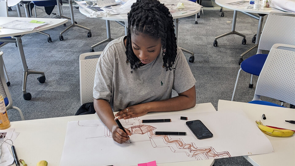 Female student sat at an architectural studio, drawing sketches.