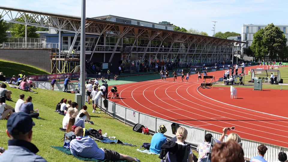Outside the Paula Radcliffe Stadium, showing the track and attendees watching on the grass banks