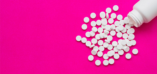Pictured is a bottle of pills on a pink background.