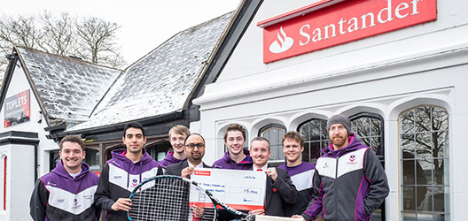 photo of some of the Tennis Foundation student volunteer coaches standing outside the University Santander branch with some of the bank staff holding a cheque 