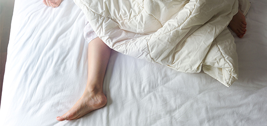 photo of a woman's feet hanging out of a duvet on a bed