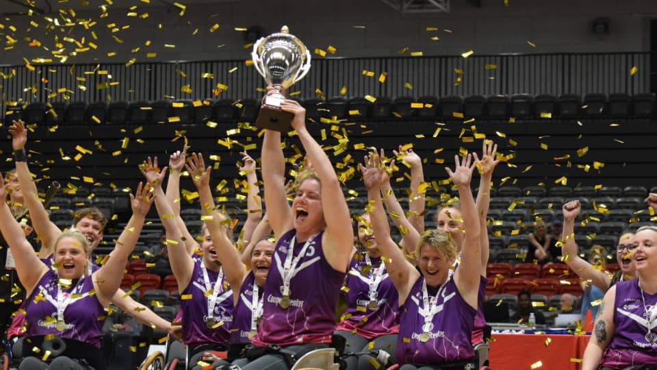 Loughborough Lightning wheelchair basketball team waving their arms above their heads and one person is holding a silver trophy in the air.