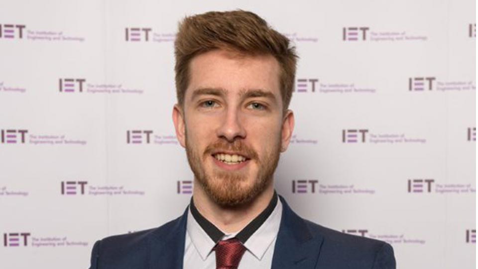 Headshot of student smiling, standing in front of a backdrop showing thee IET awards logos. 