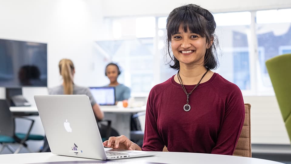 dhwani smiling at camera behind laptop