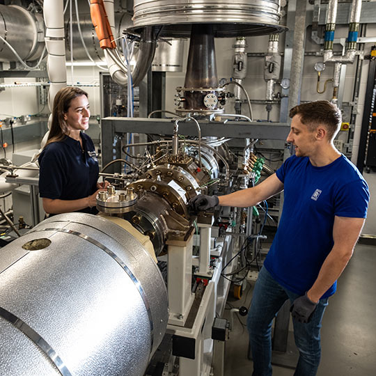 Two people in a jet engine laboratory facing each other talking