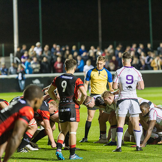 A group of rugby players in action with a crowd watching in the background