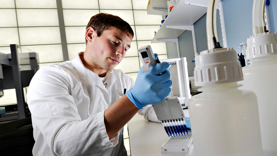 A male researcher in a white lab coat injecting blue dye into a sample dish