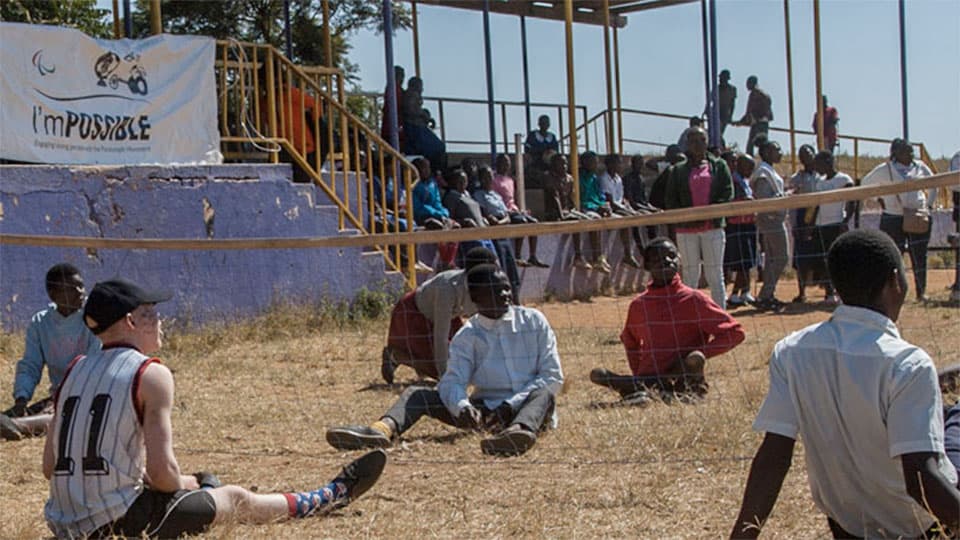 A group of young people sitting on the ground during a sports match © Photo by Amos Gumulira/Agitos Foundation.