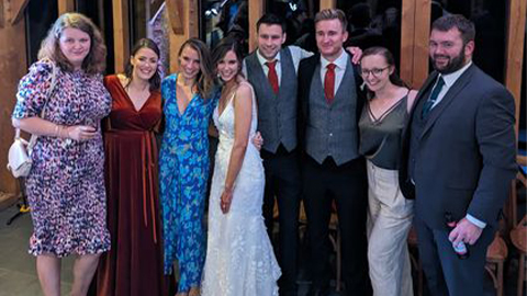 Emma and Matt smiling with a group of alumni at their wedding
