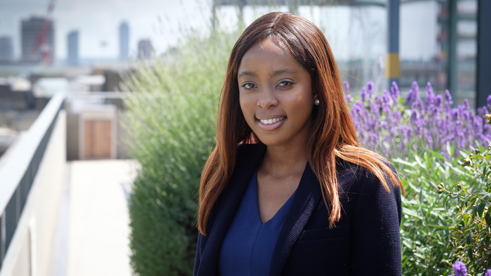 Consolata Amode standing on a balcony with plants in the background.