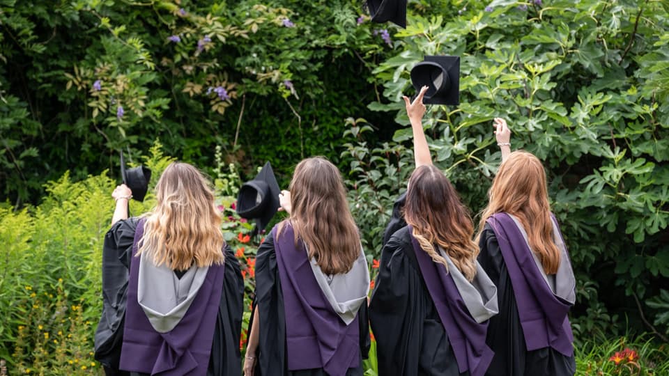 Four graduates throwing caps in the air. Their backs are facing the camera.