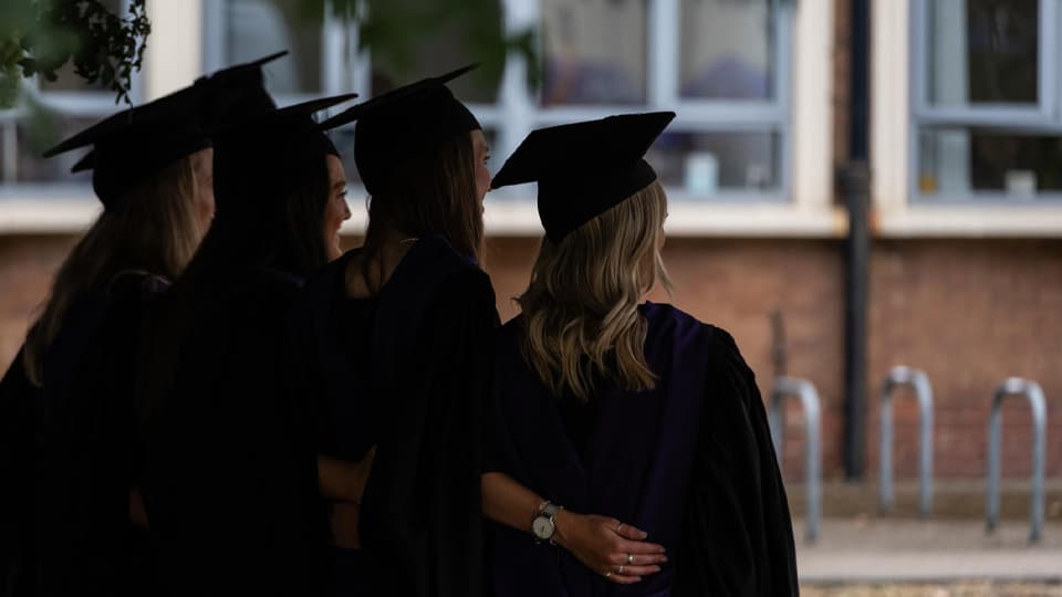 A group of graduates from the back. They are silhouettes. There are four people.