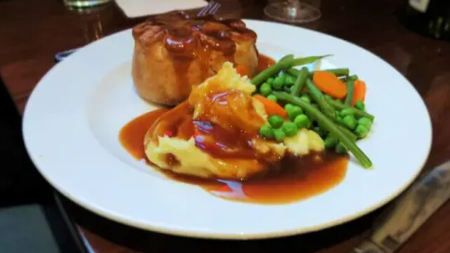 A plate of pie and mash with vegetables and gravy