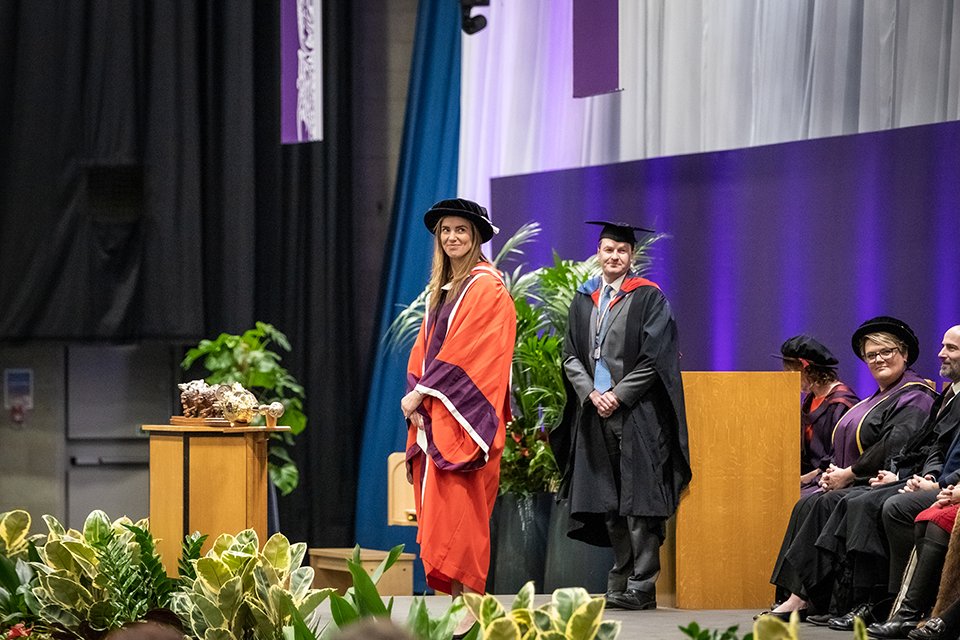 Sarah Hunter standing on stage wearing robes to receive her honorary degree