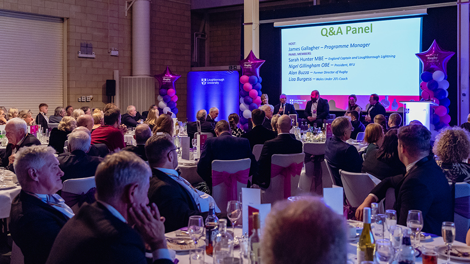 People seated at tables looking towards a stage where a panel of people sit