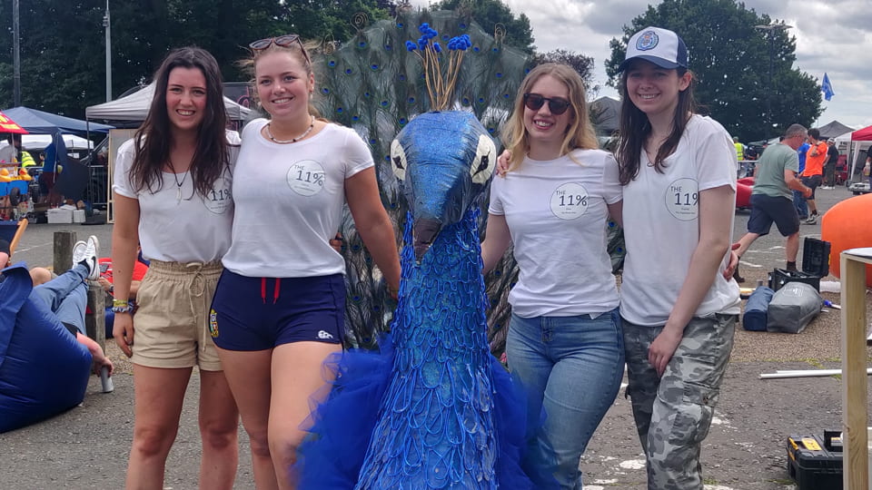 Four students standing behind their soapbox - a blue peacock