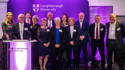 A group of people standing on stage in front of a purple banner featuring the university's logo