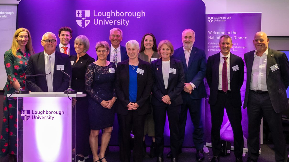 A group of people standing on stage in front of a purple banner featuring the university's logo