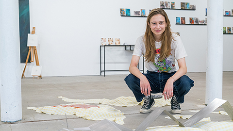 Klara crouches with materials in front of her and artwork on the walls in the background