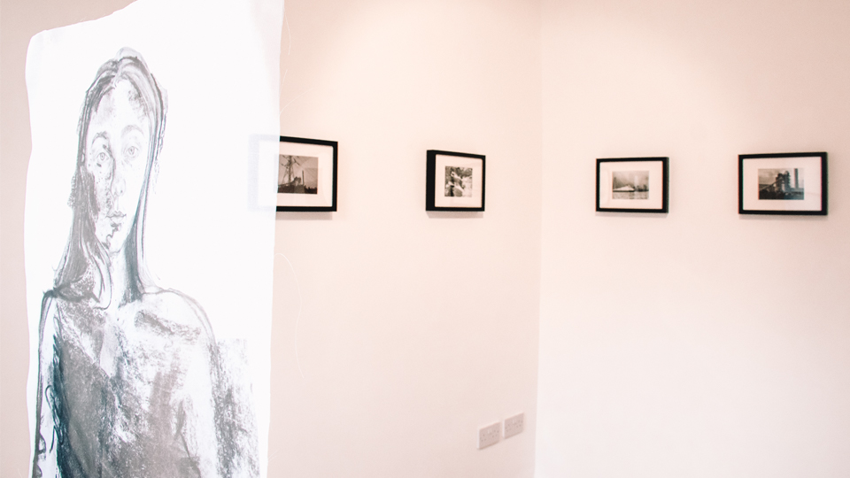 A sketched portrait of a woman with other art at the exhibition in the background