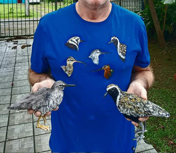 an image of the torso wearing a blue shirt with illustrations of birds of them holding two models of birds.