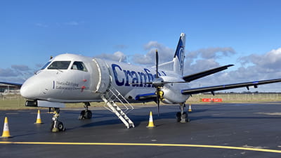 A plane standing stationary on a runway. There are yellow cones on the ground. The plane has the word “Cranfield” on the side.