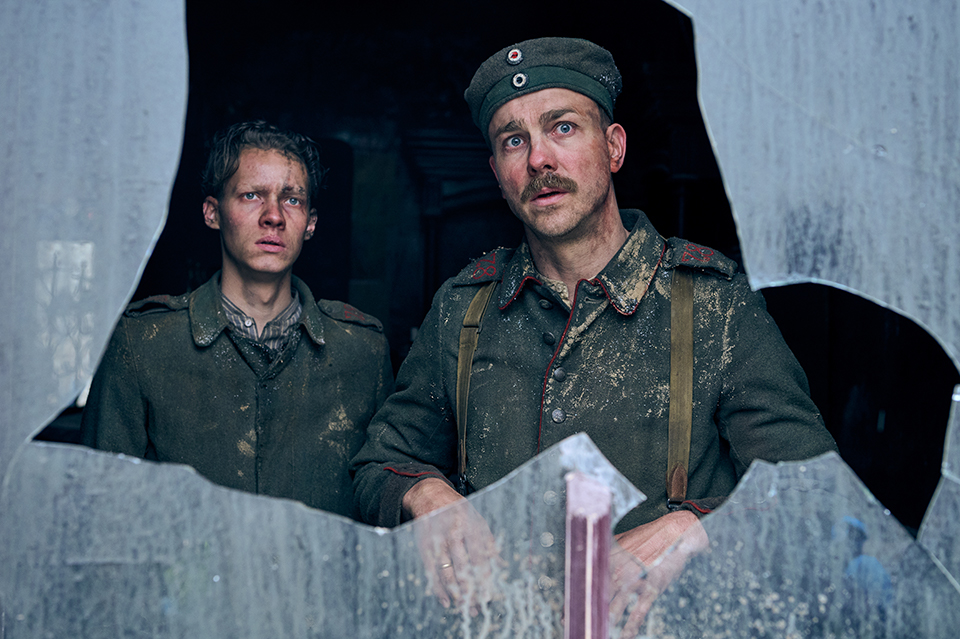 Two soldiers stand together looking through a piece of broken glass. ©ReinerBajo