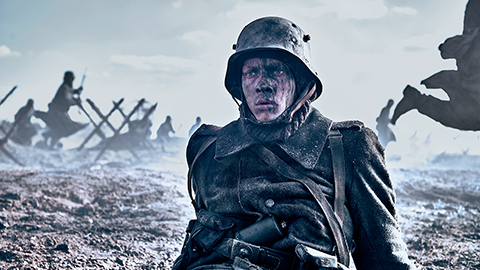 A dark image of a soldier sitting on the ground wearing uniform. His face is dirty. In the background is a war scene. Still taken from Netflix film All Quiet on the Western Front. Copywrite - ReinerBajo - Netflix.