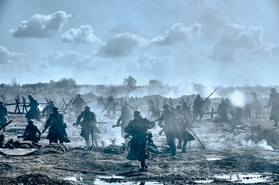 A war scene. Soldiers are seen running and carrying guns. The ground is muddy. The image is grey and dark, but the sky is quite light. Still taken from Netflix film All Quiet on the Western Front. Copywrite - ReinerBajo - Netflix.