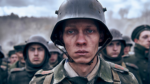 A soldier's face, head and shoulders. He looks into the distance. He is wearing uniform and a helmet. In the background there are other soldiers. Still taken from Netflix film All Quiet on the Western Front. Copywrite - ReinerBajo - Netflix.