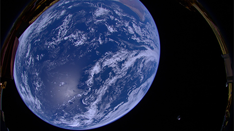 Photo of Earth from Low Earth Orbit using onboard camera on the HAKUTO-R Lunar Lander Spacecraft. 
There is an image of earth taken from space. The planet's blue colour glows against the darkness. A small grey shape is on the bottom right of the image - this is the SpaceX Falcon rocket in its second stage.