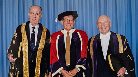 Tom Karen pictured in the centre with two other people. All are wearing graduation robes.