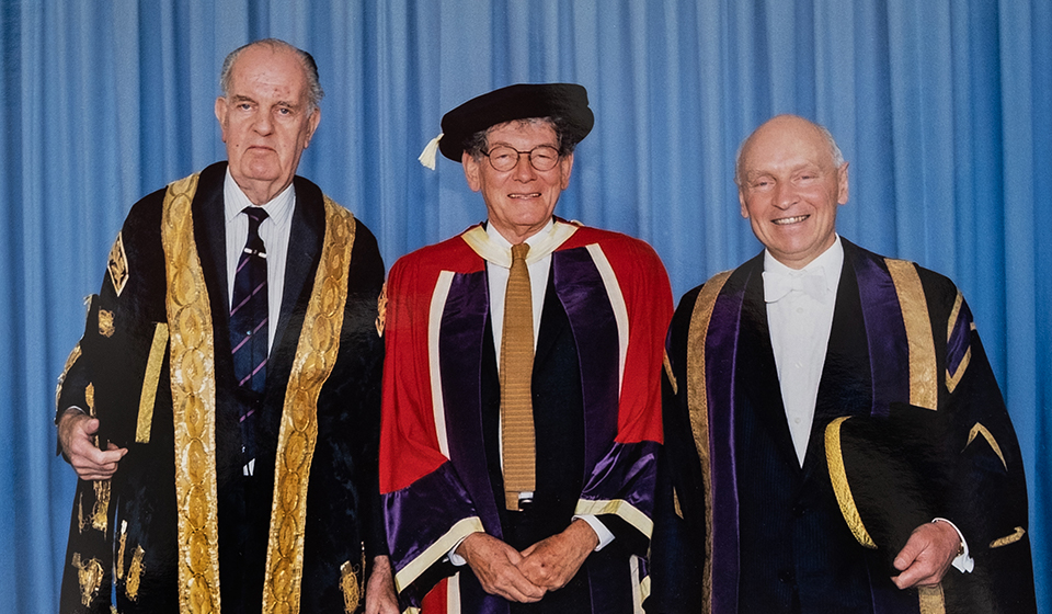 Tom Karen pictured in the centre with two other people. All are wearing graduation robes.