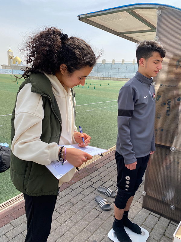 An image of Diala standing next to a sportsperson on weighing scales.