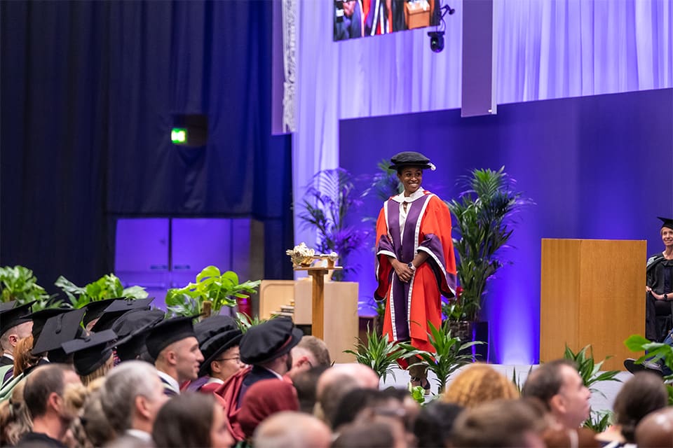 Ebony-Jewel Rainford-Brent stands on stage in front of graduates