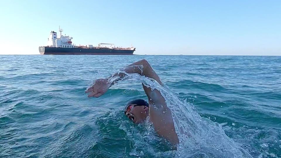 Andy Donaldson swimming in the ocean. A ship is in the distance.