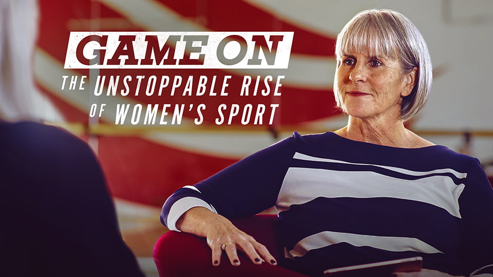 Sue Anstiss seated looking away from the camera at someone out of shot. The Game On logo is in the top left.