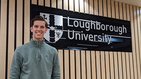 Ben Jennings stands in front of a university logo that is on a cladded wooden wall