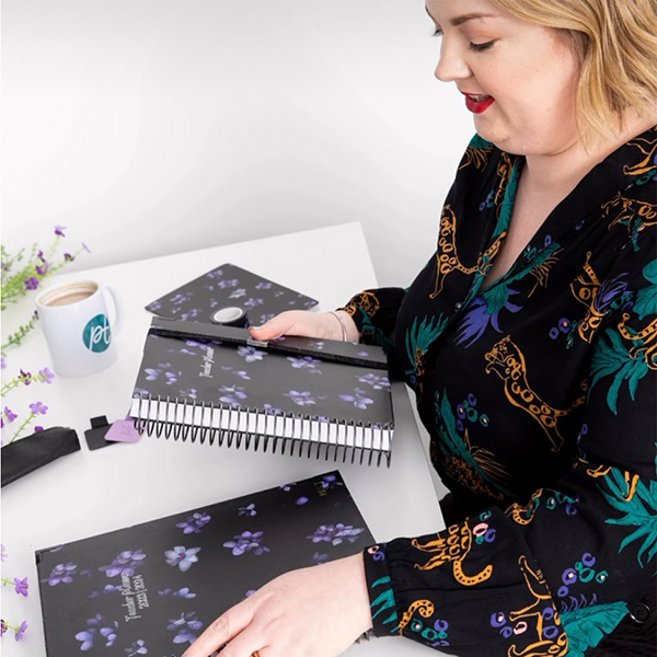 An image of Hayley standing at a desk over to journals from the Midnight Petals collection.